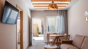 A modern living room with a sofa, a dining table with chairs, a TV mounted on the wall, and a staircase leading to an outdoor area. - Modern Luxury 2-Bed Apt, in the heart of Stalis and steps from the Beach. (Heraklion)
