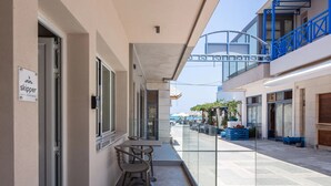 A balcony with a table and chairs, a sign for 'Skipper Cozy Apartment', and a view of the street with shops and outdoor seating. - Modern Luxury 2-Bed Apt, in the heart of Stalis and steps from the Beach. (Heraklion)