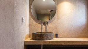 A bathroom with a stone sink, a round mirror, and a built-in shelf. - Modern Luxury 2-Bed Apt, in the heart of Stalis and steps from the Beach. (Heraklion)