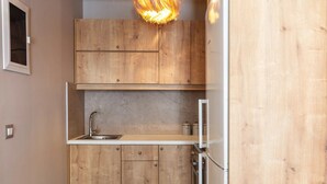 A compact kitchen with wooden cabinets, a stainless steel sink, and a modern light fixture. - Modern Luxury 2-Bed Apt, in the heart of Stalis and steps from the Beach. (Heraklion)