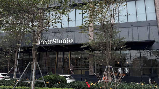 Ein modernes Gebäude mit einer großen Glasfassade, dem sichtbaren Namen 'PentStudio' und einer gepflegten Gartenanlage davor.