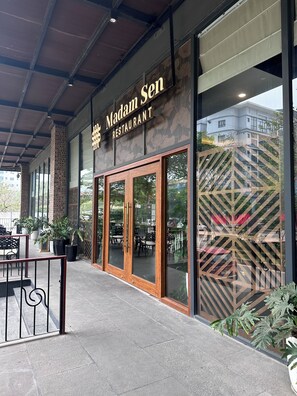 A restaurant with a sign reading 'Madam Sen Restaurant,' large glass doors, and outdoor seating with potted plants. - Muse Hanoi PentStudio West Lake (Hanoi)