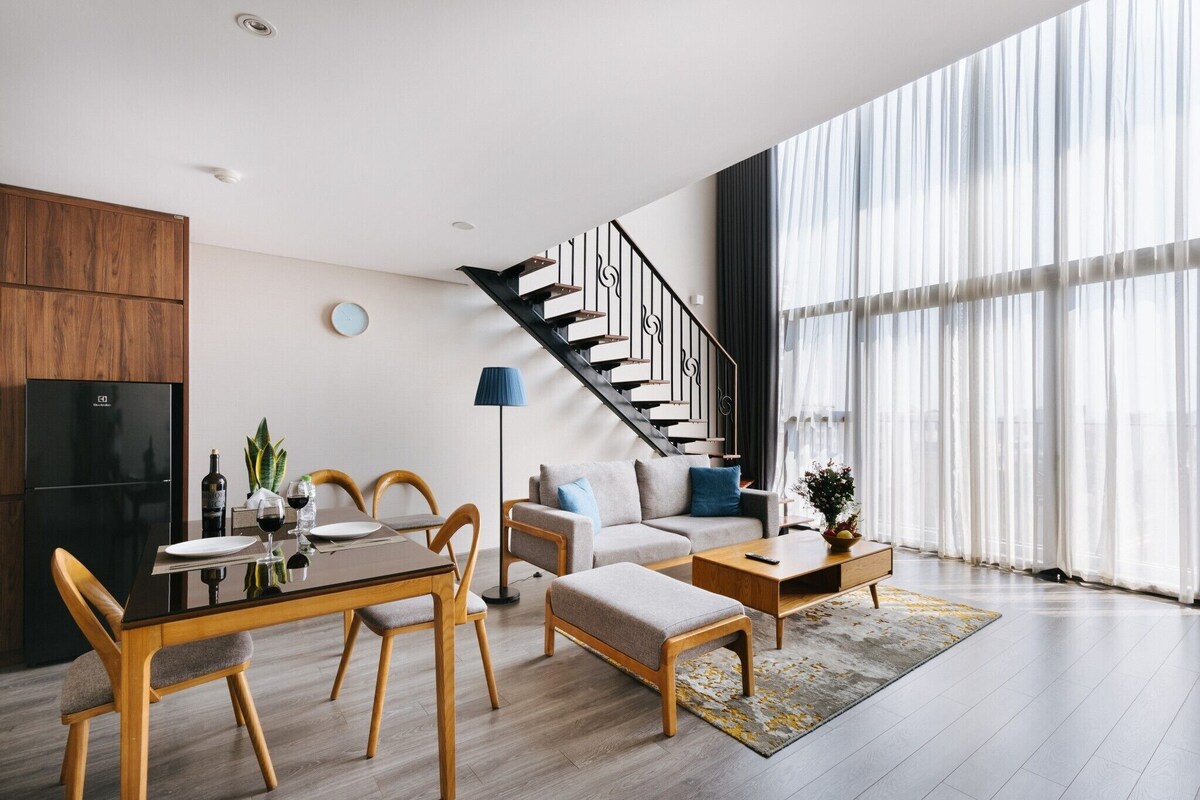 A modern living room with a dining area, a staircase, and large windows.