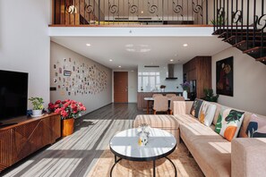 A modern living room with a sofa, coffee table, and a TV. There's a staircase leading to an upper level. - Muse Hanoi PentStudio West Lake (Hanoi)