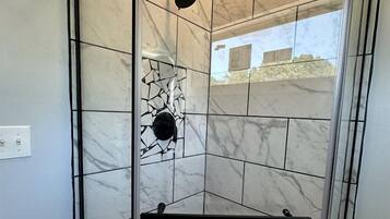 A glass-enclosed shower with a black shower head, a white floor, and a marble-tiled wall.