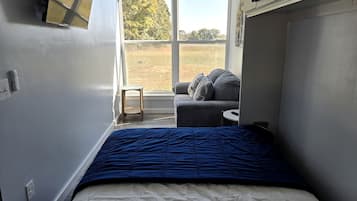 Une chambre à coucher avec un lit, une petite table, une chaise et une fenêtre donnant sur un champ.
