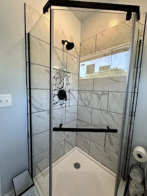 A glass-enclosed shower with a black shower head, a white floor, and a marble-tiled wall.