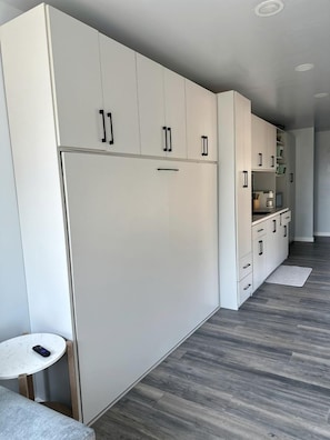 A modern kitchen with white cabinets, a built-in oven, and a small round table.