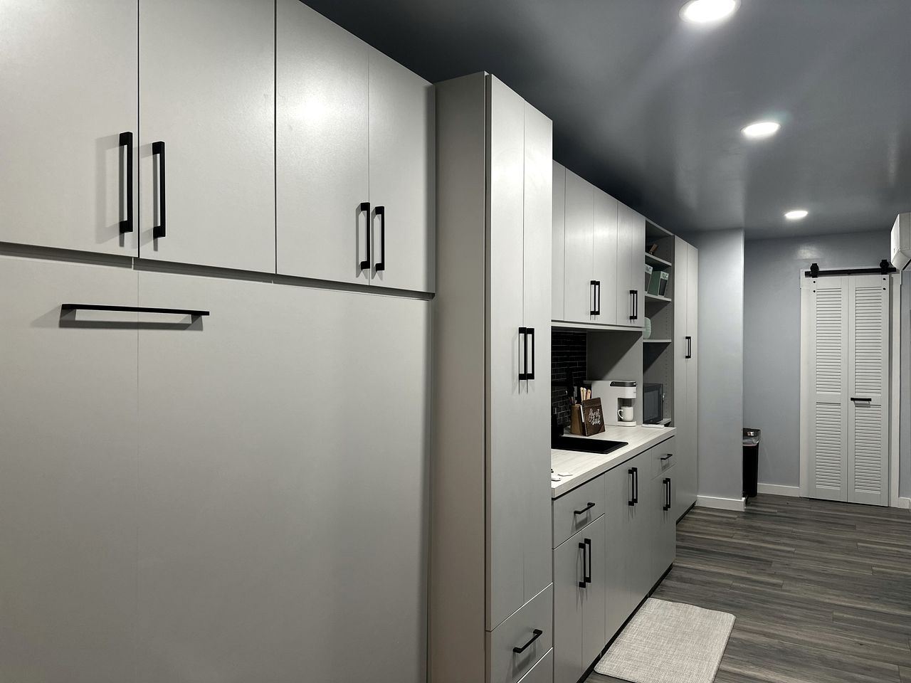 A modern kitchen with grey cabinetry, black handles, and a wooden floor.