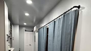 A narrow hallway with a wooden floor, a white door at the end, and a blue curtain on the right.