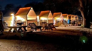 A row of tents with tables and chairs, set up in a campsite at night.