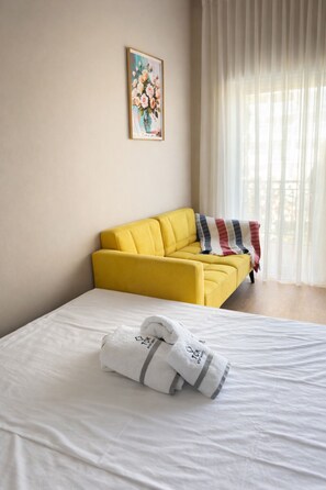 Ein Hotelzimmer mit Bett, gelber Couch, einem Bild an der Wand und einem Fenster mit Vorhängen.