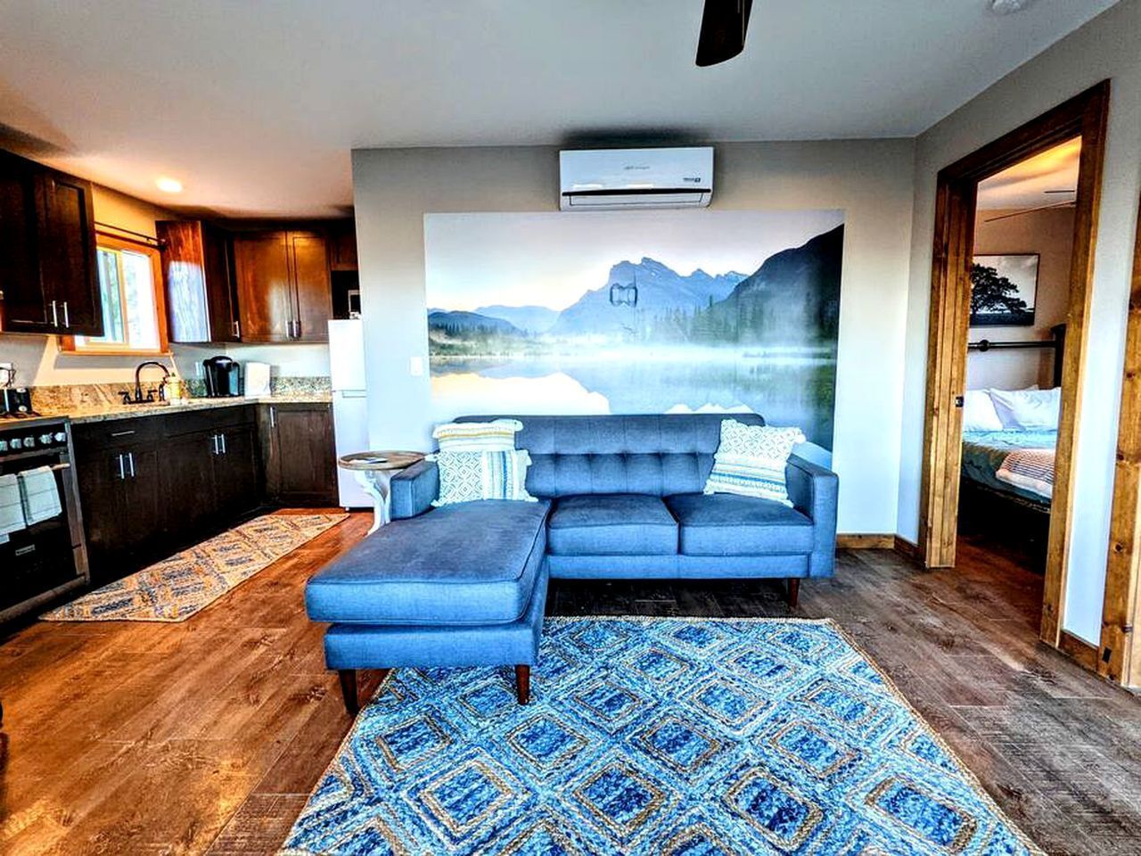A modern living room with a sectional sofa, a large painting, and a kitchen in the background.