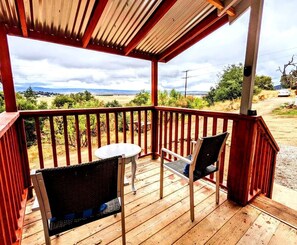 Terraza de madera con una mesa y dos sillas, con vistas a un paisaje rural.