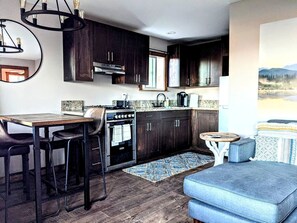 Cocina compacta con armarios de madera oscura, una isla central, estufa y un comedor con taburetes.