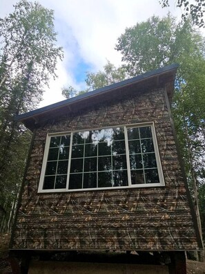 A wooden cabin with a large window, surrounded by trees. - Peaceful Tiny Cabin Escape With Onsite Play Area Close To River Adventures in Houston, Alaska (Houston)