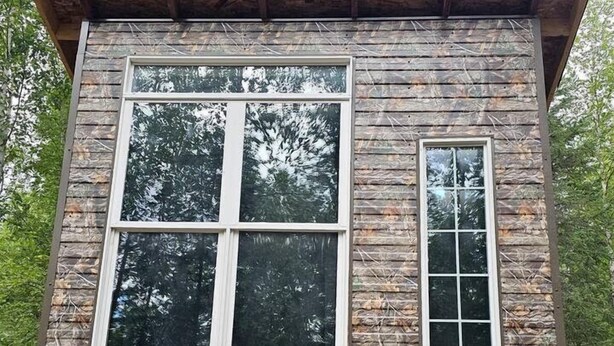 A small cabin with a single large window and a smaller window on the side, built on stilts.