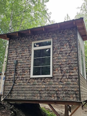 A rustic cabin with a single window, surrounded by dense foliage. - Peaceful Tiny Cabin Escape With Onsite Play Area Close To River Adventures in Houston, Alaska (Houston)
