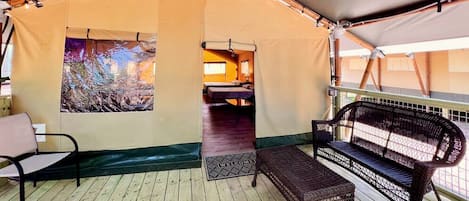 A tented accommodation with a wooden deck, a bench, a bed, and a view of a forest.