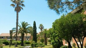 A pathway leading through a well-maintained garden with palm trees and other greenery, surrounded by buildings with a consistent architectural style. - Coastal AC Stay Near Bravone for 4 (Linguizzetta)
