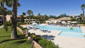 A resort pool area with lounge chairs, palm trees, and resort buildings in the background. - Coastal AC Stay Near Bravone for 4 (Linguizzetta)