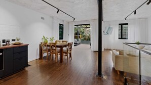 Une cuisine moderne avec un plancher en bois, un coin repas avec une table et des chaises, et une balustrade en verre donnant sur un jardin.
