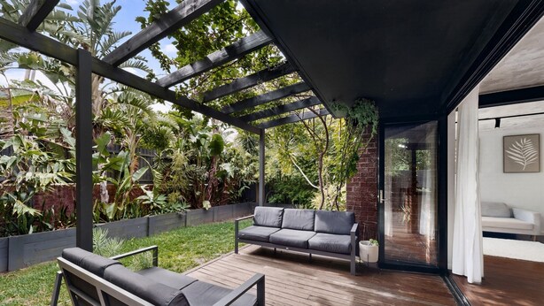 Une terrasse couverte avec un plancher en bois, deux canapés gris et diverses plantes.