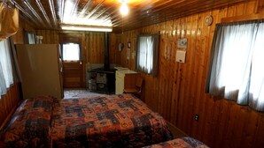 Une chambre de style cabane équipée de deux lits, d’un bureau, d’une chaise et d’un poêle.