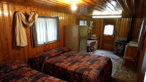 Une cabane comprenant deux lits, un coin cuisine, un espace repas et une cheminée.