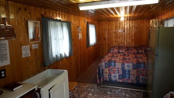 A cabin with a bed, a small kitchenette, a window with curtains, and a ceiling fan.