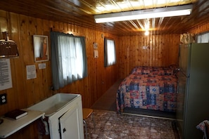 A cabin with a bed, a small kitchenette, a window with curtains, and a ceiling fan. - Remote and Cozy Mountain Cabin Nestled in the Poudre Canyon, Perfect for a Pet Friendly Glamping Retreat (Bellvue)