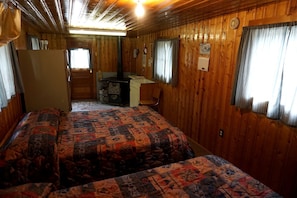 A cabin-style room with two beds, a desk, a chair, and a stove. - Remote and Cozy Mountain Cabin Nestled in the Poudre Canyon, Perfect for a Pet Friendly Glamping Retreat (Bellvue)