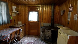 L’intérieur d’une cabane en bois, avec une table à manger, des chaises, un poêle et une fenêtre.