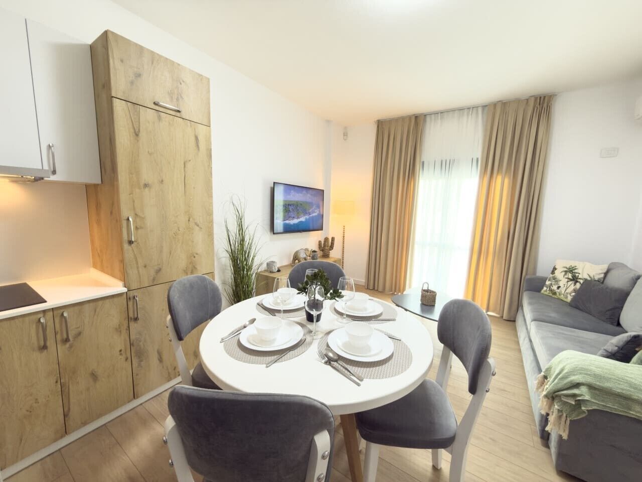 A modern living room with a dining table set for four, a grey sofa, and a wooden cabinet.