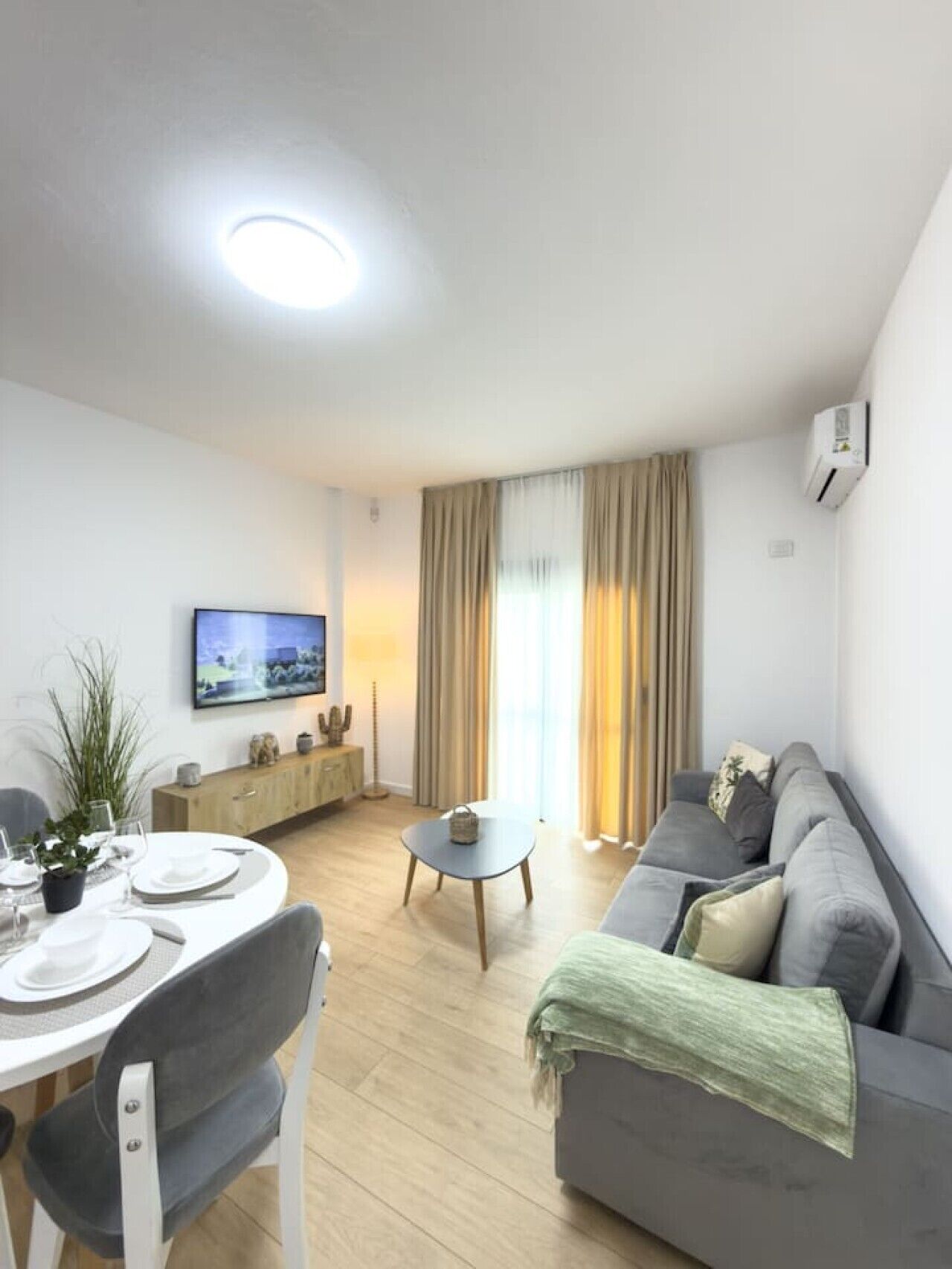 A modern living room with a dining area, a sofa, a TV, and a ceiling light.