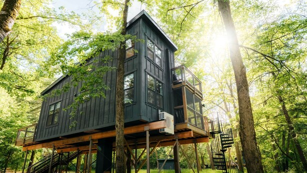 A treehouse with multiple levels, built on stilts, surrounded by a forest.