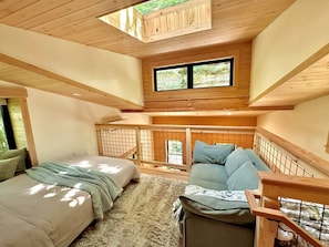 Un dormitorio estilo loft con techo alto, dos camas, un sofá y vistas al exterior a través de una ventana.