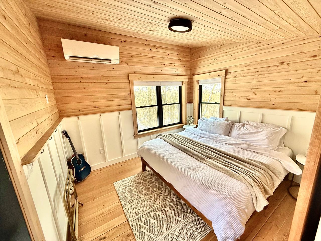 Ein Schlafzimmer mit Holzwänden, einem Bett, einer Gitarre und einem Fenster.