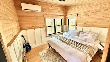 Ein Schlafzimmer mit Holzwänden, einem Bett, einer Gitarre und einem Fenster.