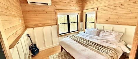 Un dormitorio con paneles de madera, una cama, una guitarra y una ventana.