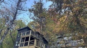 Une cabane en bois dotée d’un balcon, entourée d’arbres et d’une falaise rocheuse.