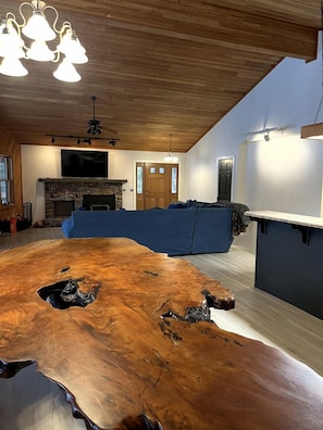 Ein modernes Wohnzimmer mit einem Holzesstisch, einem Steinkamin, einem blauen Sofa und einer Küchenzeile.