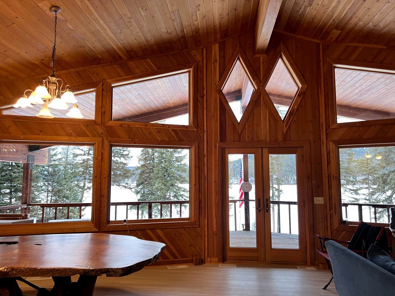 A wooden cabin with large windows, a dining table, and a view of a snowy landscape.