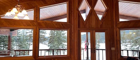 A wooden cabin with large windows, a dining table, and a view of a snowy landscape.
