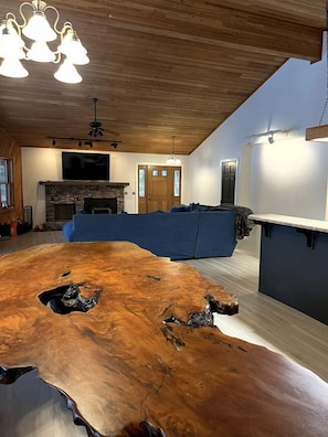 Ein modernes Wohnzimmer mit einem Holzesstisch, einem Steinkamin, einem blauen Sofa und einer Küchenzeile.
