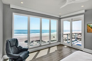 Ein Zimmer mit großen Fenstern und Blick auf den Strand, ein moderner Sessel und ein Bett.