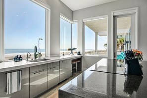 Eine moderne Küche mit einer großen Kochinsel, Blick auf den Strand und einem Essbereich mit Außenbestuhlung.