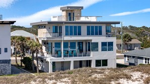 Ein mehrstöckiges Strandhaus mit Balkon, großen Fenstern und einem turmartigen Anbau.