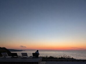 A sunset view from a wooden deck with lounge chairs facing the sea.