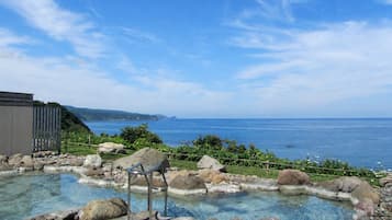 A clear pool with rocks and a metal chair, surrounded by a stone deck, overlooking a body of water and distant land.